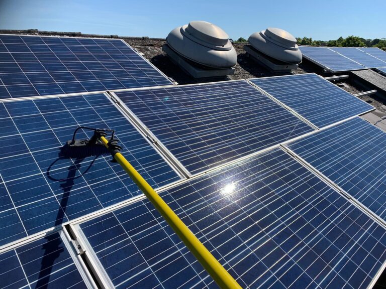 A long yellow pole with a brush cleaning solar panels on a rooftop under a clear blue sky, showcasing vibrant sunlight reflections.