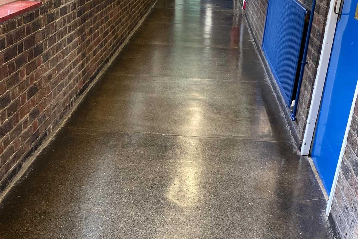 Shiny, polished floor in a narrow hallway with brick walls and a blue door at the far end, conveying a clean and inviting atmosphere.