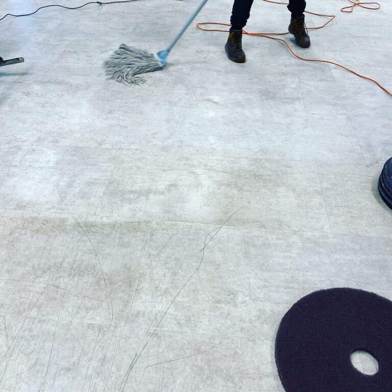 A person mops a light-colored floor with a blue mop, while electric cords and weight plates are visible nearby.