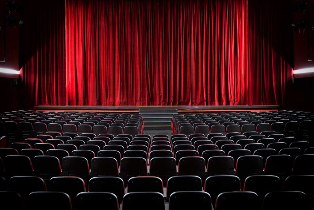 A theater interior featuring red curtains and rows of black seats.